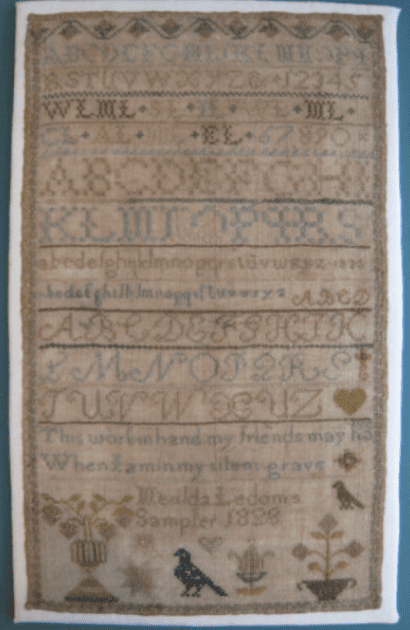 Rectangular linen sampler embroidered with rows of alphabets, decorative borders, floral motifs, and a stitched inscription with a date from the 1800s.